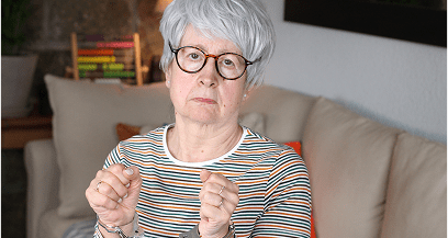 Elderly woman with glasses sitting on sofa.
