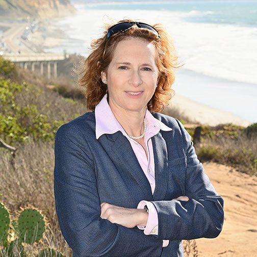 Woman standing outdoors near the coast with arms crossed.